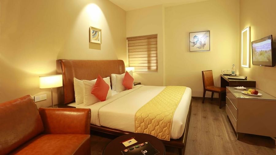 Executive Room at Mayberry Tiruppur with a bed, TV stand with a wall-mounted TV, a table with a chair, and a sofa